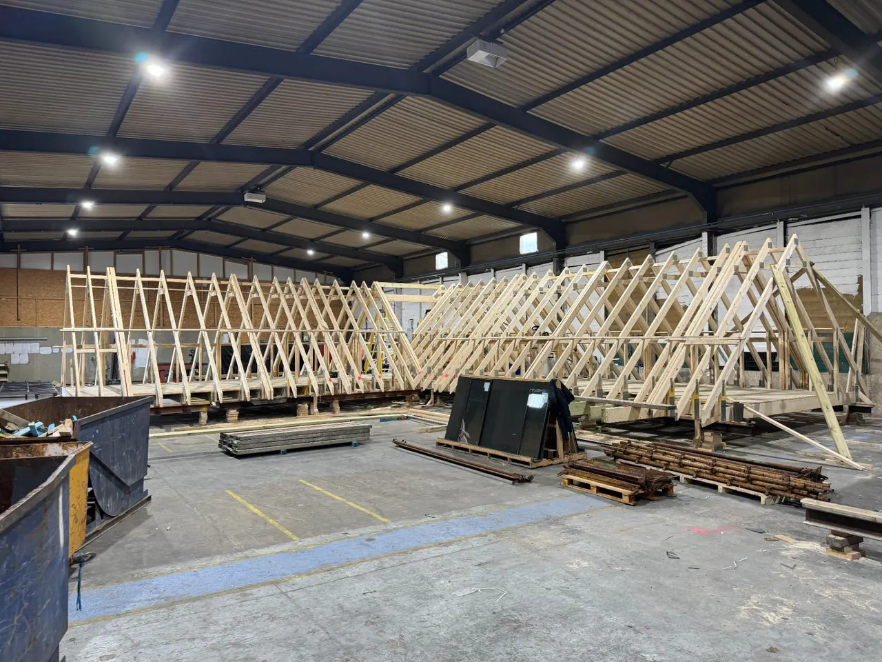 Multiple trussed roof structures lined up across the factory floor, mid-build